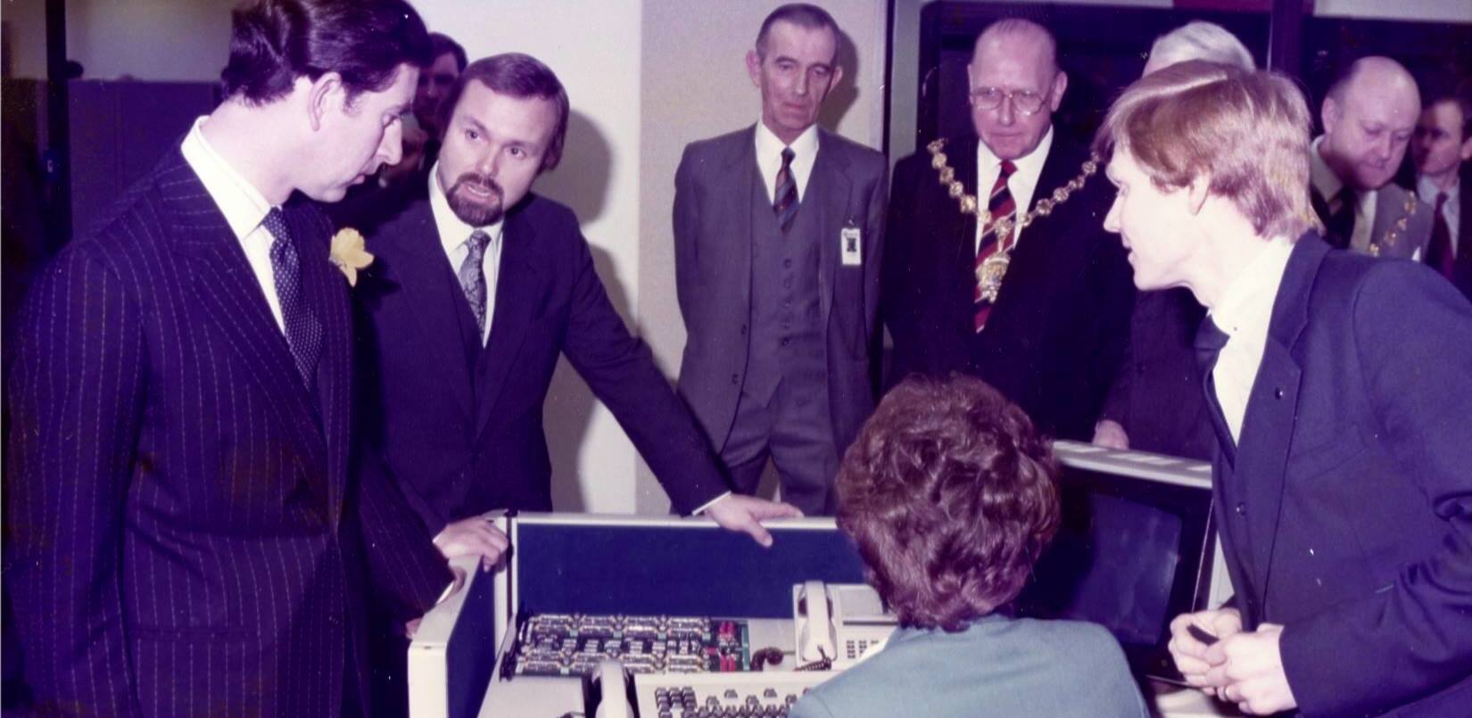 Terry Matthews présente les travaux de Mitel au prince Charles lors de sa visite dans l'entreprise en 1983. 